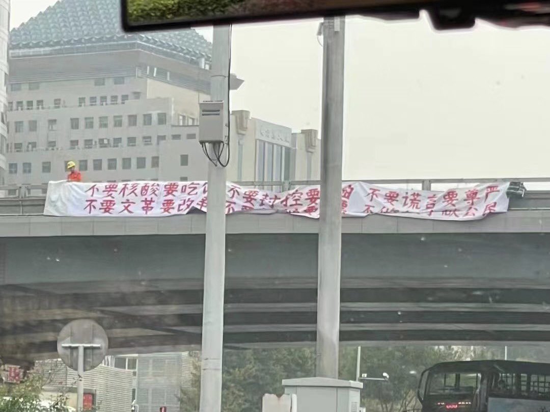 2022年10月13日，北京四通桥，身穿橙色工作服的抗议者在桥上悬挂白底红字政治横幅。与封面不同画面｜来源：China Change／2022年10月14日刊载